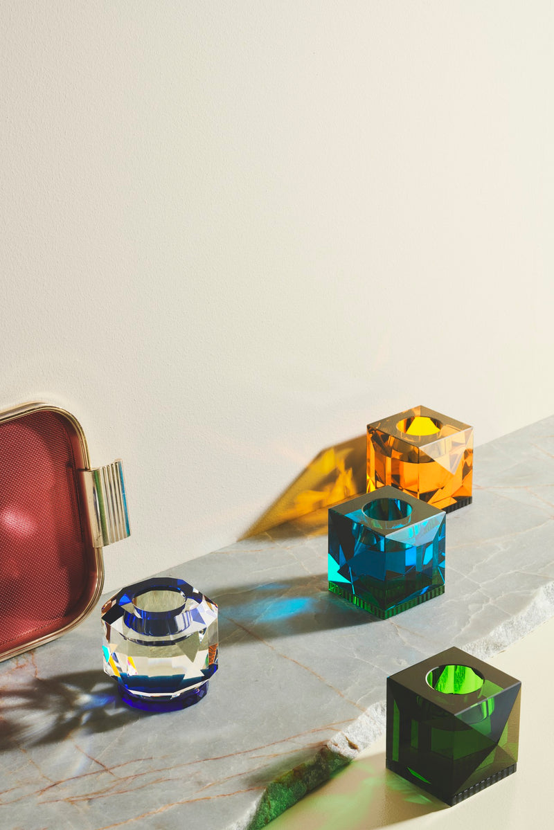 Fire forskellige fyrfadslysestager i farvet krystal, på marmorplade.