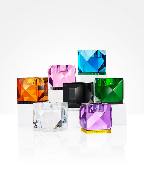 Opstilling af syv forskellige fyrfadslysestager i farvet krystal, på hvid baggrund.