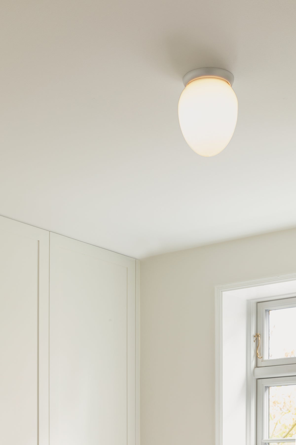 Loftlampe med sølvfarvet fatning og skærm af opalglas, på hvidt loft