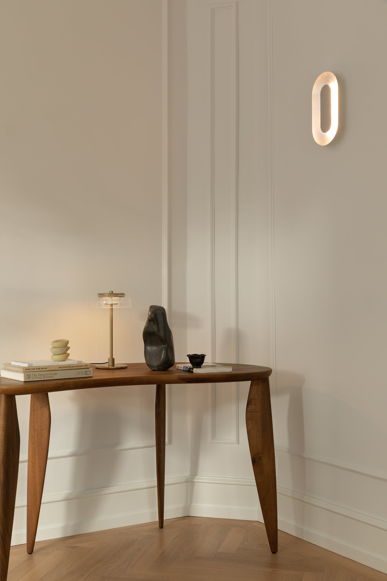 Oval sølvfarvet væglampe med indirekte lyskilde, på hvid væg i kontor